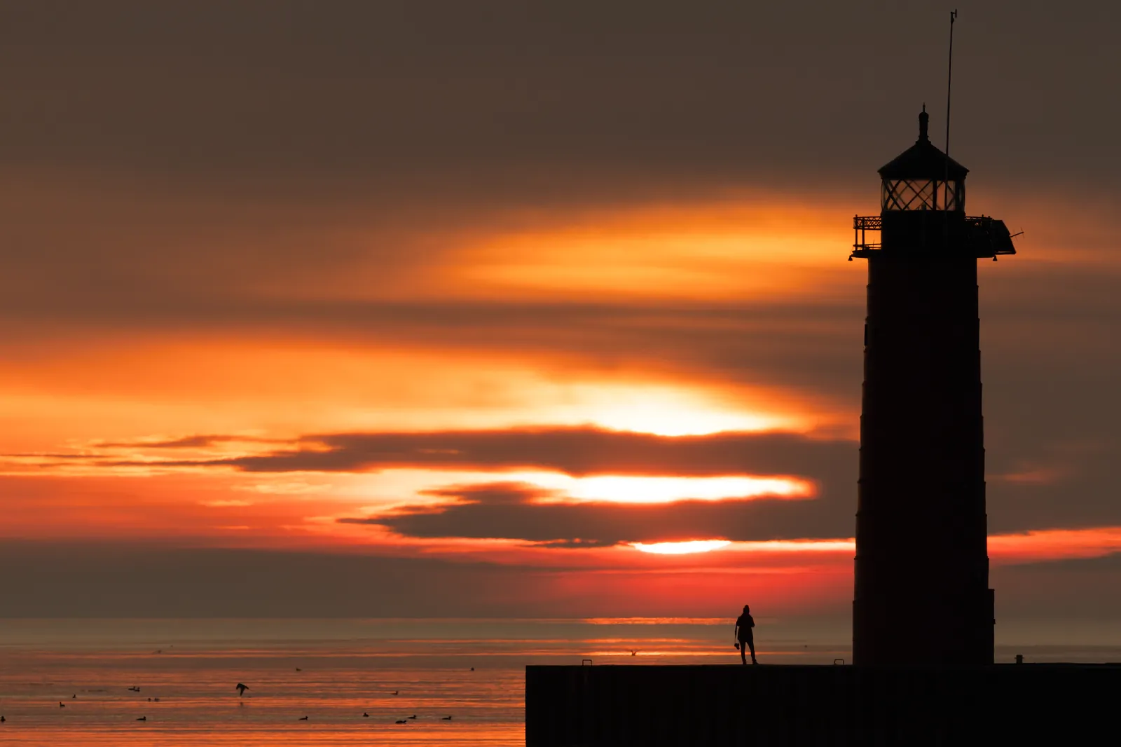 Sunrise over Lake Michigan with a lighthouse pier and a lone figure watching the light